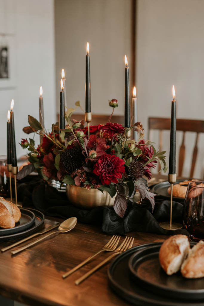 Dramatic Thanksgiving tablescape featuring black taper candles in brass holders surrounded by burgundy dahlias and roses, paired with dark plates, smoked glasses, and a luxe moody fall vibe.