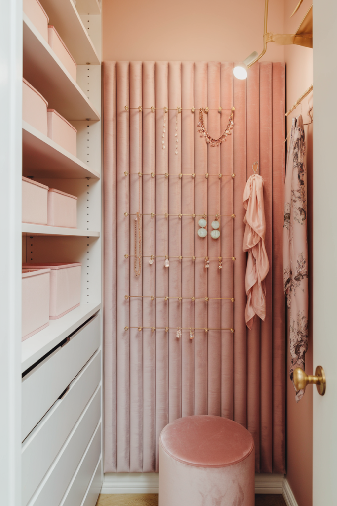 Small luxury closet with sensor-lit drawers showing blush camisoles, pearl jewelry, and soft neutral knits in organized compartments.