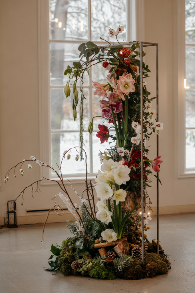 Tall vertical installation of white amaryllis, hellebores and trailing eucalyptus on a black iron frame with mossed base.