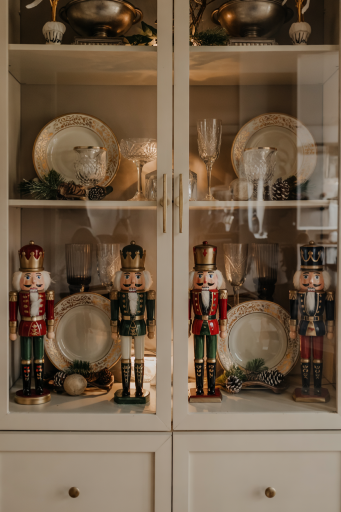 Nutcracker figurines displayed with holiday dishes and glassware inside a modern china cabinet.