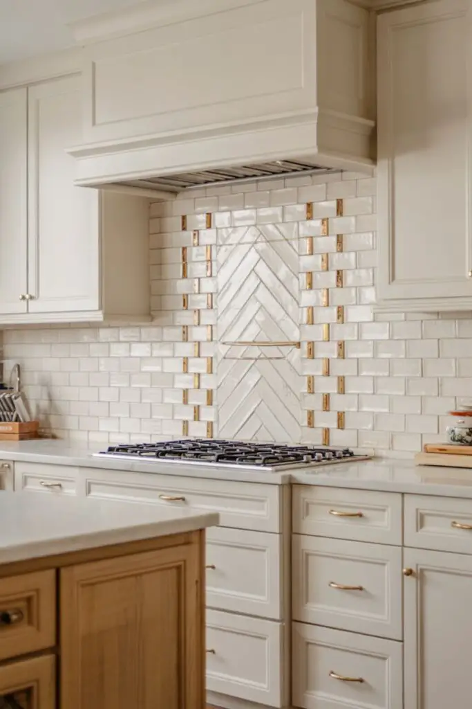 Bright modern transitional kitchen featuring a mixed-material statement backsplash of matte white subway tiles with brushed-brass and marble mosaic accent strips in a subtle herringbone pattern.