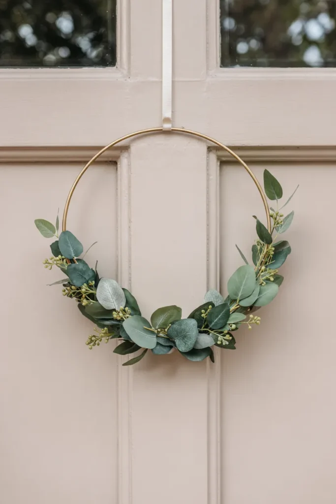 Minimalist eucalyptus hoop wreath on a thin metal ring hanging on a closed front door, styled in a calm and cozy modern spring aesthetic.